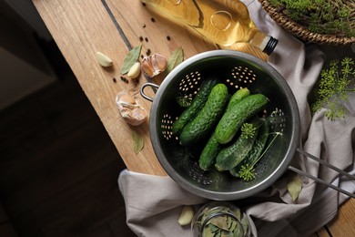 Fresh cucumbers in colander and other ingredients prepared for canning on wooden table, flat lay. Space for text