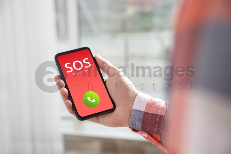 Man holding smartphone with emergency call SOS on screen indoors, closeup