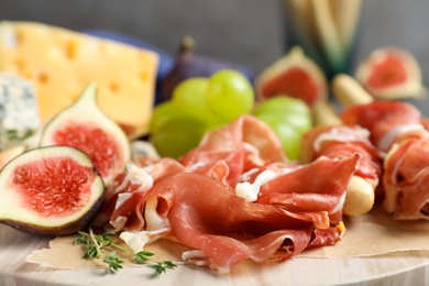 Photo of Board with delicious figs, cheese, grapes and bread with proscuitto, closeup