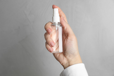 Photo of Woman holding antiseptic spray on light grey background, closeup