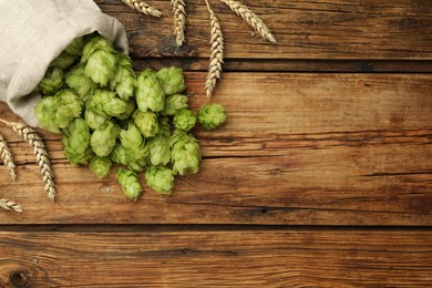 Photo of Sack with fresh green hops and wheat ears on wooden table, flat lay. Space for text