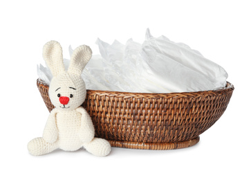 Wicker bowl with disposable diapers and toy bunny on white background