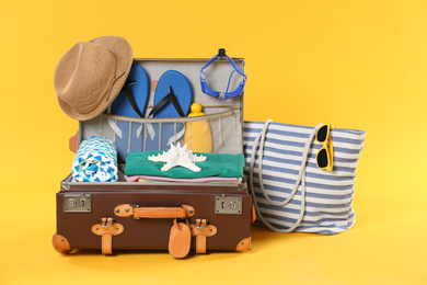 Bag and open vintage suitcase with different beach objects packed for summer vacation on orange background