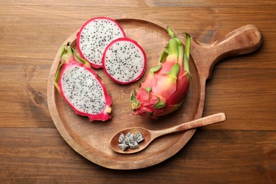Serving board of delicious cut and whole white pitahaya fruits with spoon on wooden table, top view