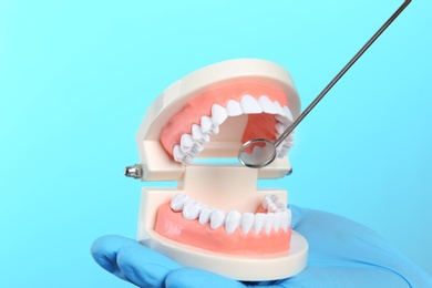 Dentist showing how to exam teeth with educational model of oral cavity and mouth mirror on color background