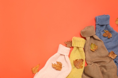 Warm sweaters and dry leaves on orange background, flat lay with space for text. Autumn season