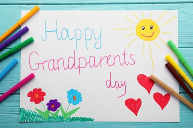 Beautiful drawing with phrase Happy Grandparents Day on blue wooden table, flat lay