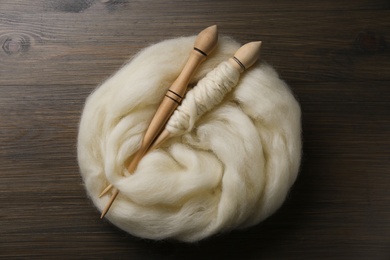 Soft white wool and spindles on wooden table, flat lay