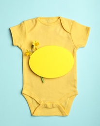 Child's bodysuit, flowers and card with space for text on light blue background, top view