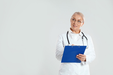 Mature doctor with clipboard on light grey background. Space for text