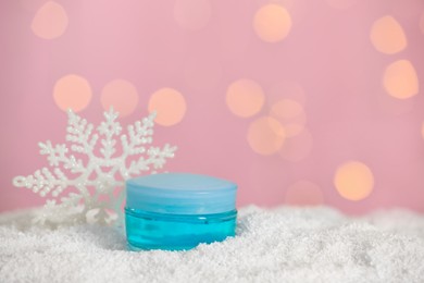 Jar of hand cream and decorative snowflake on snow against blurred lights, space for text. Winter skin care