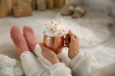 Woman holding cup of delicious drink with whipped cream and marshmallows indoors, closeup. Christmas celebration