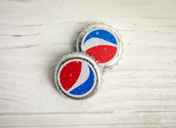 MYKOLAIV, UKRAINE - FEBRUARY 11, 2021: Pepsi lids with water drops on white wooden table, flat lay