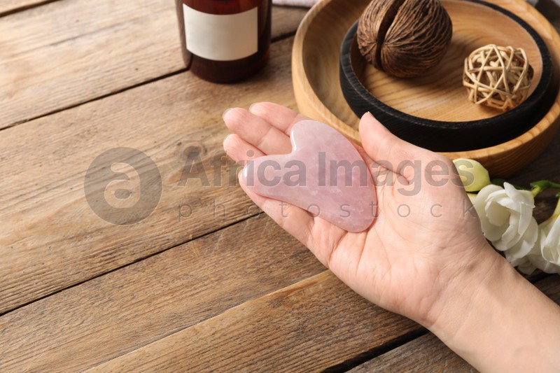 Photo of Woman holding gua sha tool at wooden table, closeup. Space for text