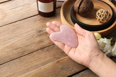Photo of Woman holding gua sha tool at wooden table, closeup. Space for text