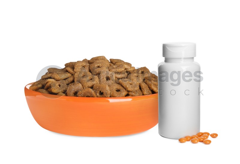 Dry pet food in feeding bowl and bottle with vitamin pills on white background