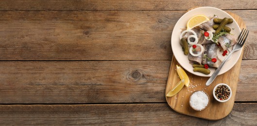 Image of Salted herring fillets served with thyme, pickles, onion rings, chili pepper and lemon on wooden table, top view with space for text. Banner design