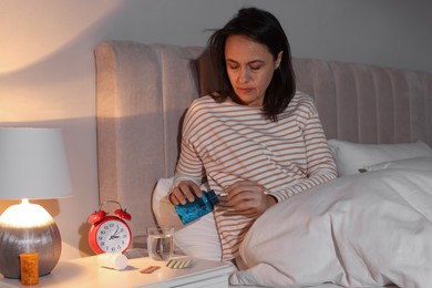 Mature woman with bottle of pills suffering from insomnia in bed at night