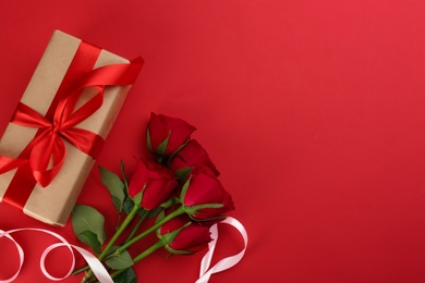 Beautiful gift box and roses on red background, flat lay with space for text. Valentine's day celebration