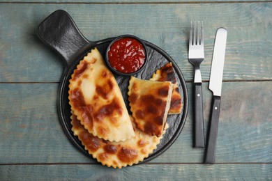 Delicious fried chebureki with ketchup served on light blue wooden table, flat lay