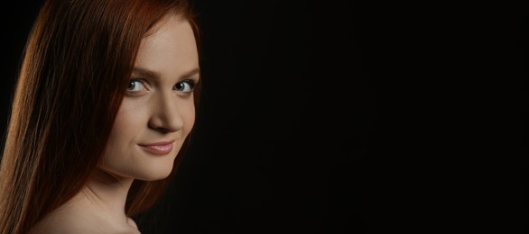 Candid portrait of happy young woman with charming smile and gorgeous red hair on dark background, space for text