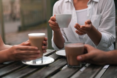 Photo of Friends drinking coffee and cocoa at wooden table in outdoor cafe, closeup