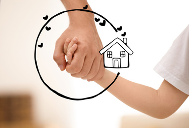 Father holding hands with child and illustration of house indoors, closeup. Adoption concept