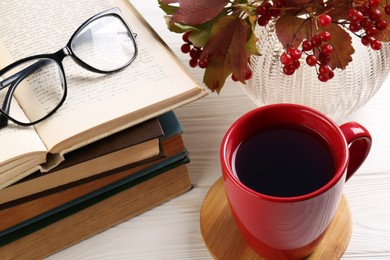 Cup with hot drink, stack of books and glasses on white wooden table, above view. Autumn atmosphere