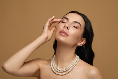 Young woman wearing elegant pearl jewelry on brown background
