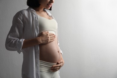 Pregnant young woman touching belly on light background, closeup. Space for text