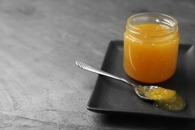 Delicious orange marmalade in jar and spoon on grey table. Space for text