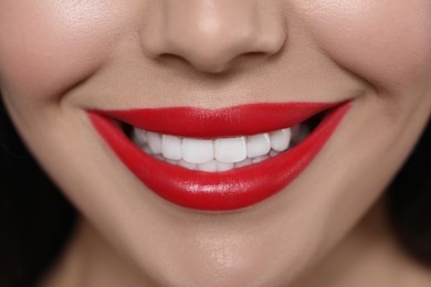 Young woman wearing beautiful red lipstick on dark background, closeup