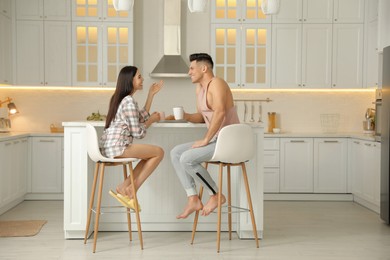 Photo of Happy couple wearing pyjamas during breakfast at table in kitchen