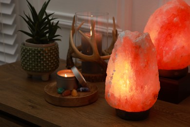 Himalayan salt lamps, candles, houseplant and gemstones on wooden table near white wall indoors