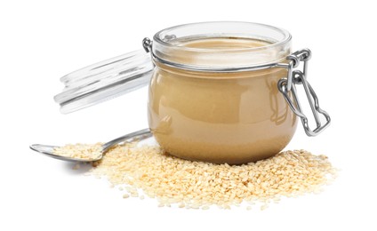 Tasty sesame paste in jar, spoon and seeds on white background