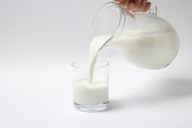Woman pouring milk into glass on white background, closeup