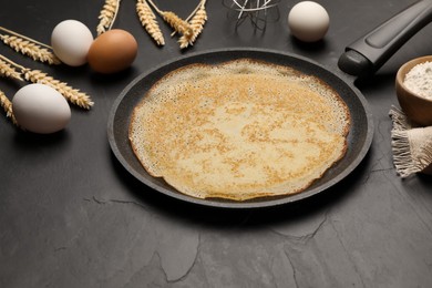 Photo of Frying pan with delicious crepe, spikelets and ingredients on black table