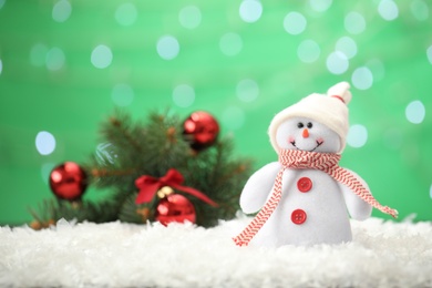 Snowman toy on snow against blurred festive lights, space for text. Christmas decoration
