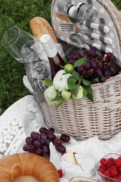 Picnic blanket with tasty food, flowers, basket and cider on green grass outdoors