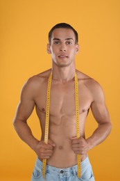 Handsome shirtless man with slim body and measuring tape on yellow background