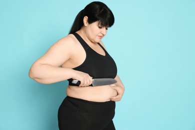 Obese woman with knife on light blue background. Weight loss surgery