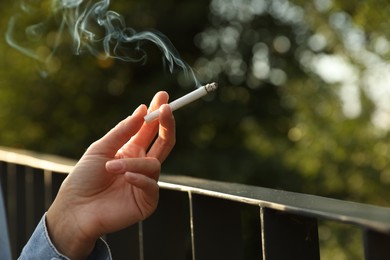 Photo of Woman smoking cigarette near railing outdoors, closeup of hand. Space for text