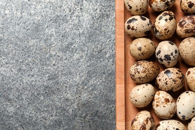 Wooden tray with quail eggs on grey table, top view. Space for text