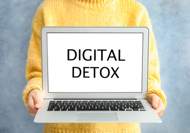 Woman holding laptop with phrase DIGITAL DETOX on light blue background, closeup