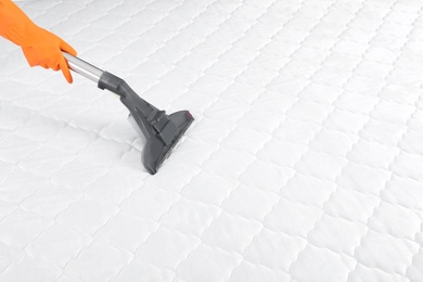 Person disinfecting mattress with vacuum cleaner, closeup. Space for text