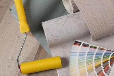 Wall paper rolls, color palette and tool on wooden floor, above view