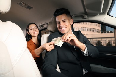 Photo of Young woman giving money taxi driver in modern car