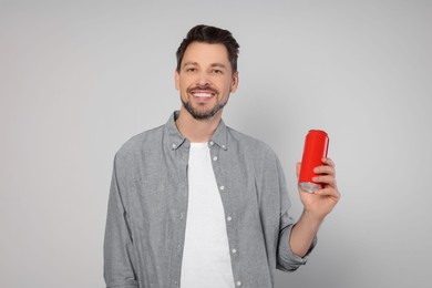 Photo of Happy man holding red tin can with beverage on light grey background