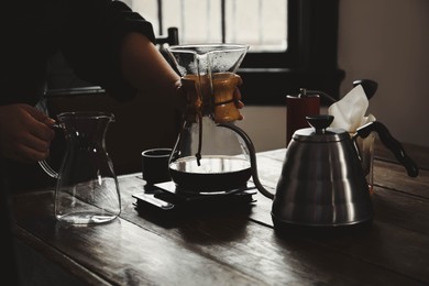 Photo of Barista with coffee maker and jug at wooden table in cafe, closeup