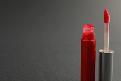 Photo of Red lip gloss with applicator on dark background, closeup. Space for text